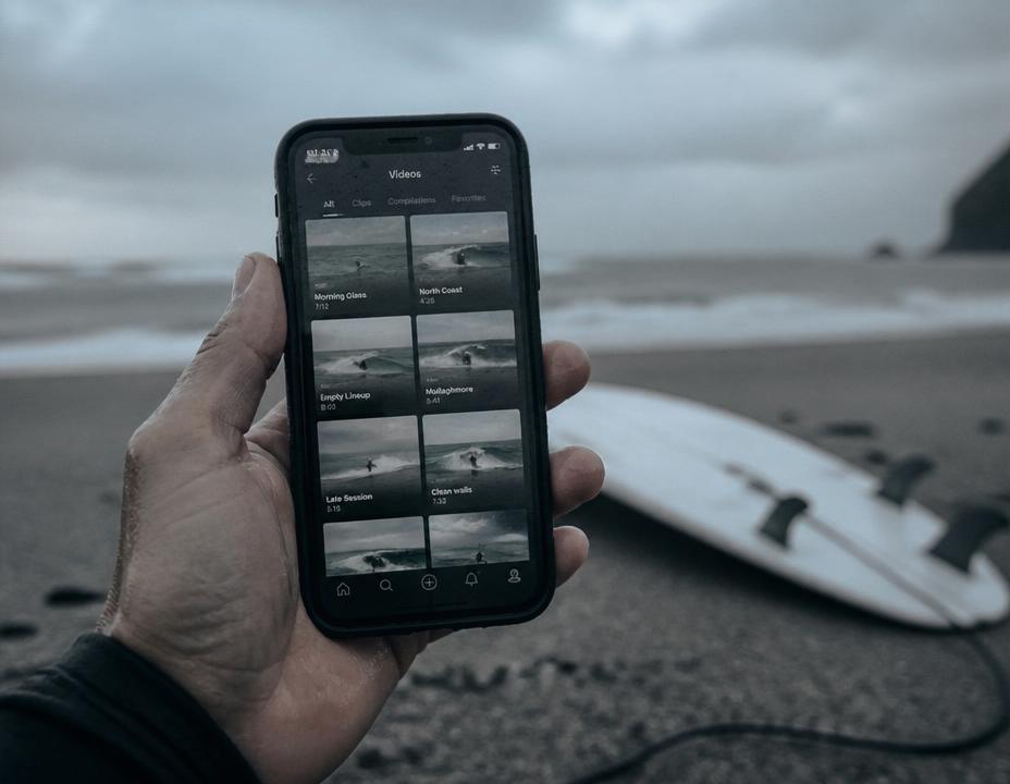 A phone on the beach showing a grid of surf video clips